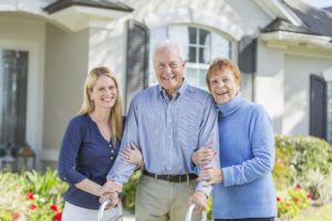 man with walker walking beside daughter and wife in front of house